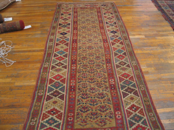 Tan, red, and blue runner rug featuring stylized floral motifs and geometric borders on light wood flooring.