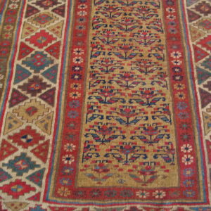 Detailed runner rug displaying geometric and stylized floral patterns in red, gold, blue, and brown on a wood floor.
