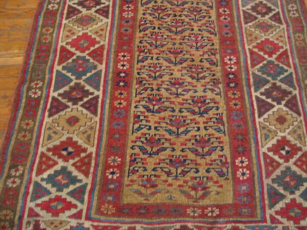 Detailed runner rug displaying geometric and stylized floral patterns in red, gold, blue, and brown on a wood floor.
