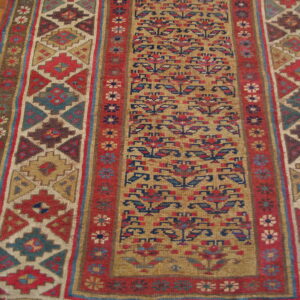 Flatweave runner features geometric borders and a floral field in red, blue, and tan on wood flooring.