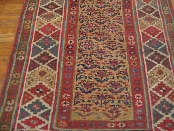 Flatweave runner features geometric borders and a floral field in red, blue, and tan on wood flooring.