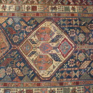 Close-up of a tightly woven rug showing geometric diamond motifs in navy, coral, cream, and brown.
