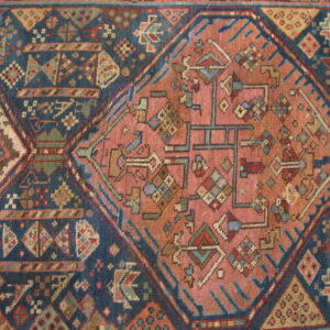 Muted pink geometric medallion centered on a dark blue rug with intricate tribal designs and accent colors.