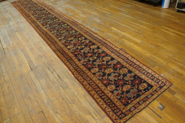 Dark blue geometric runner rug with red and gold accents lies on distressed wood flooring.
