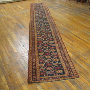 Long low-pile runner featuring a dark blue field and repeating colorful geometric patterns on hardwood flooring.