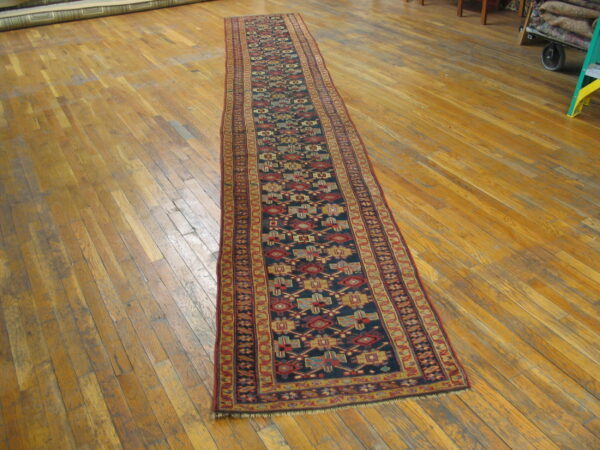 Long low-pile runner featuring a dark blue field and repeating colorful geometric patterns on hardwood flooring.