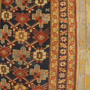 Navy, red, and gold geometric rug detail with a striped border placed on distressed wooden floorboards.