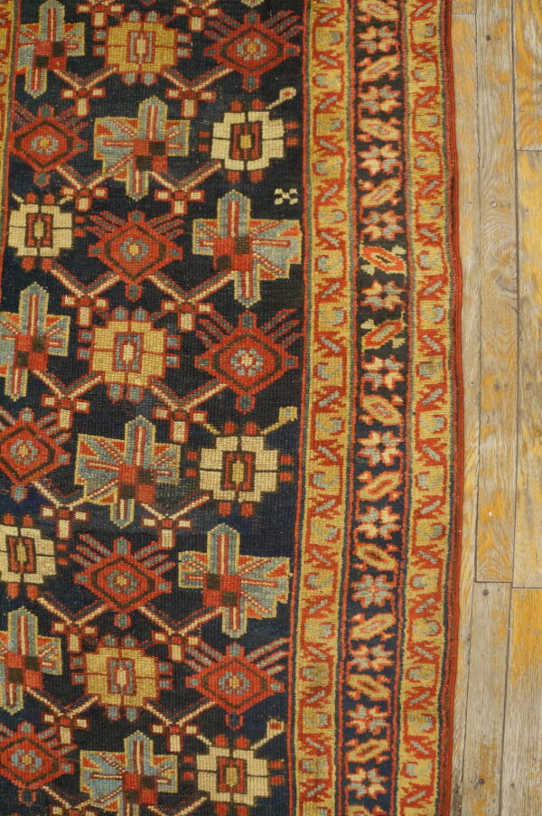 Navy, red, and gold geometric rug detail with a striped border placed on distressed wooden floorboards.