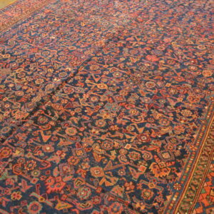 A richly patterned low-pile rug featuring a navy field and geometric motifs in rust, orange, and teal on a wood floor.