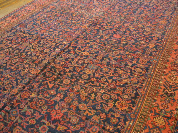 A richly patterned low-pile rug featuring a navy field and geometric motifs in rust, orange, and teal on a wood floor.