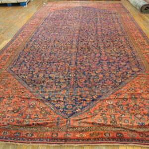 Oversized rug with a dense blue field and rust-red patterned spandrels rests on wood flooring.