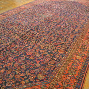 A large, low-pile rug featuring dense geometric patterns in navy, rust, and teal on wood flooring.