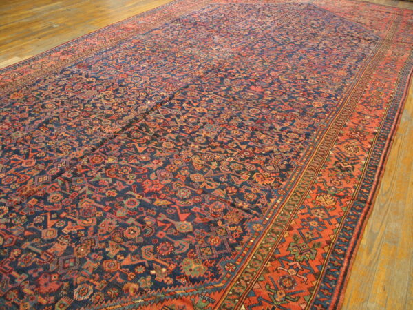 A large, low-pile rug featuring dense geometric patterns in navy, rust, and teal on wood flooring.