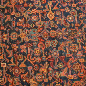 Close-up of a low-pile rug featuring dense geometric patterns in navy, orange, and teal.