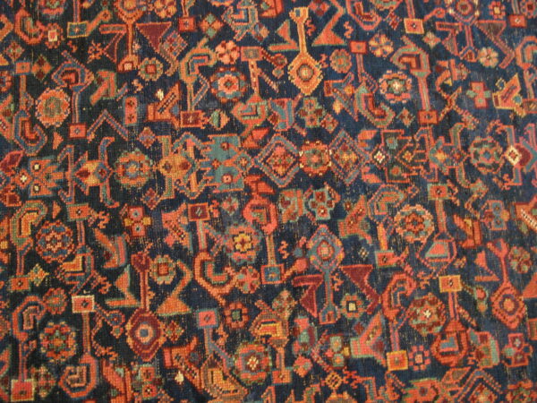 Close-up of a low-pile rug featuring dense geometric patterns in navy, orange, and teal.