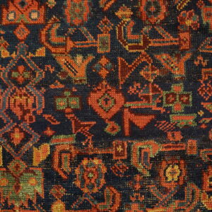 Intricate geometric rug pattern featuring a navy blue field contrasted with red, orange, and teal motifs.