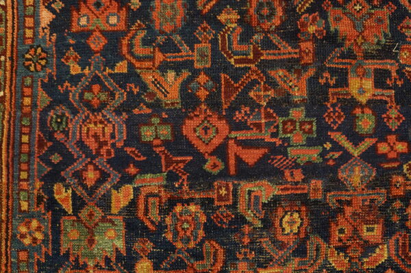 Intricate geometric rug pattern featuring a navy blue field contrasted with red, orange, and teal motifs.