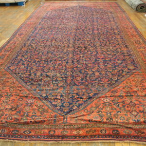 Intricate low-pile rug with a navy center and wide rust border displayed flat on wooden flooring.