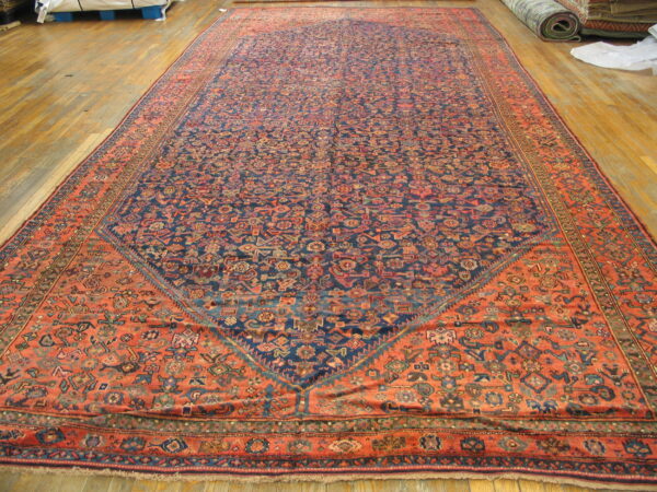 Intricate low-pile rug with a navy center and wide rust border displayed flat on wooden flooring.