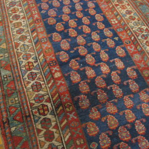 Dark blue rug with repeating red paisley motifs and intricate multi-color geometric borders over wood flooring.