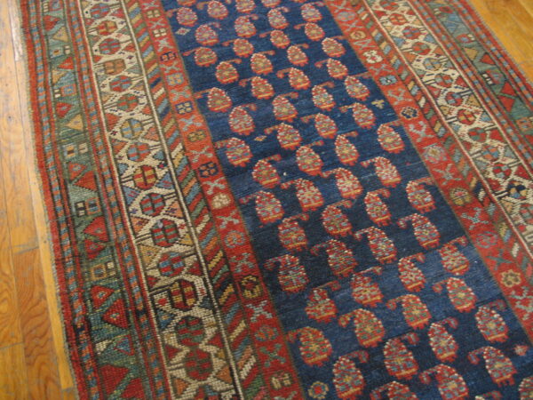 Dark blue rug with repeating red paisley motifs and intricate multi-color geometric borders over wood flooring.