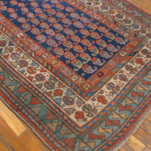 Close-up of a blue and red patterned rug featuring ornate geometric borders resting on polished wood floors.