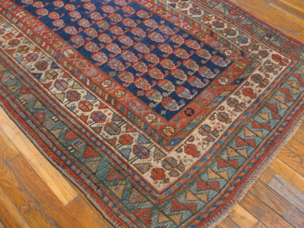 Close-up of a blue and red patterned rug featuring ornate geometric borders resting on polished wood floors.