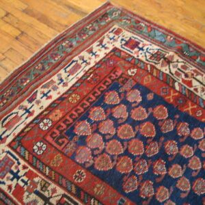 A navy blue rug with repeating red geometric motifs and complex borders rests on light brown hardwood planks.