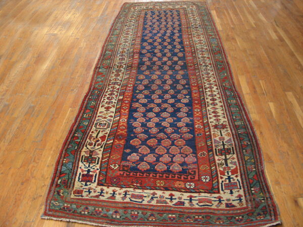 Narrow runner rug with a navy field, repeating red designs, and complex borders, lying on light wood flooring.