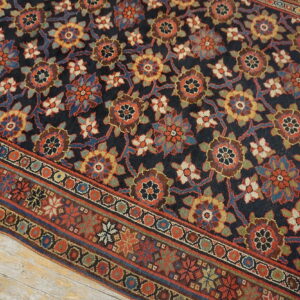 Navy and multi-color floral patterned rug displayed on distressed light wood plank flooring.