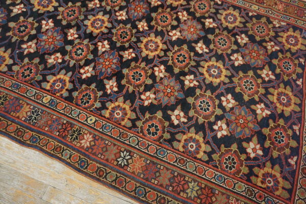 Navy and multi-color floral patterned rug displayed on distressed light wood plank flooring.