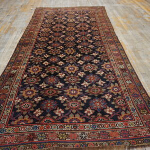 Dark runner rug with repeating multicolored medallions and thick borders rests on light wooden plank flooring.