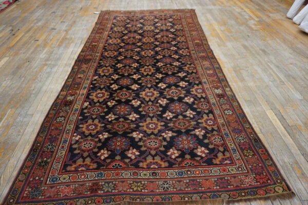 Dark runner rug with repeating multicolored medallions and thick borders rests on light wooden plank flooring.