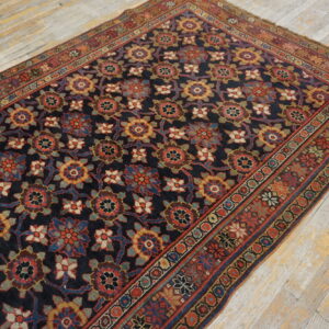 A dark blue rug with repeating multicolor floral patterns rests on distressed wooden floorboards.