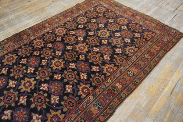 A dark blue rug with repeating multicolor floral patterns rests on distressed wooden floorboards.