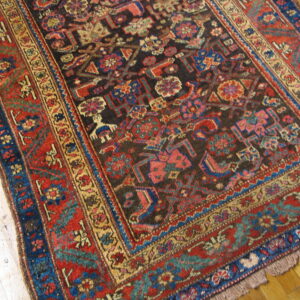 Dark-field traditional rug featuring detailed red, blue, green, and tan geometric patterns on hardwood.