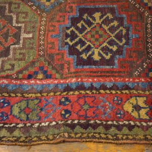 Geometric rug border and field in muted red, blue, green, and brown, laid on wood floorboards.
