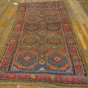 Geometric runner rug in red, blue, and earth tones with repeating medallions on wood planks.