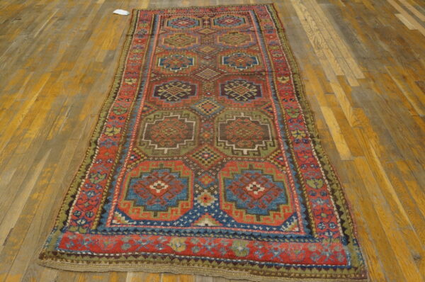 Geometric runner rug in red, blue, and earth tones with repeating medallions on wood planks.