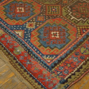 Geometric patterned rug corner showing red, blue, and green motifs against worn wooden flooring.