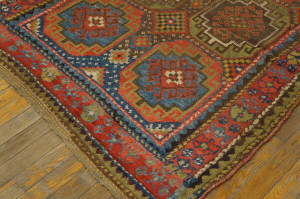 Geometric patterned rug corner showing red, blue, and green motifs against worn wooden flooring.