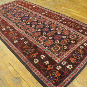 A dark blue rug with maroon borders and geometric floral patterns lies on light wooden floorboards.