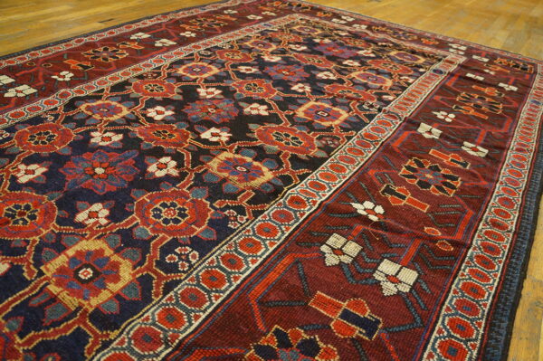 Deep red and navy rug with repeating stylized floral patterns and multiple geometric borders on hardwood flooring.