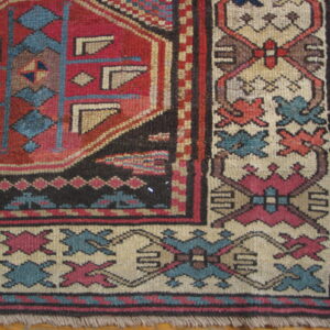 Geometric red, teal, and beige patterned rug corner with visible fringe rests on hardwood flooring.