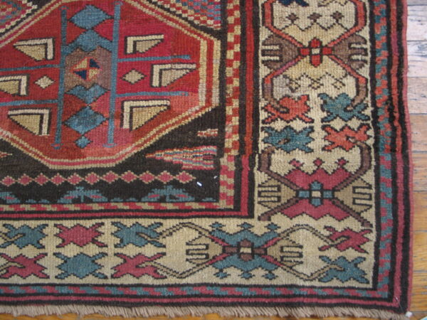 Geometric red, teal, and beige patterned rug corner with visible fringe rests on hardwood flooring.