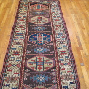Traditional geometric runner rug featuring cream, blue, and red patterns on a dark field over wood floors.