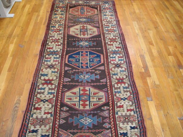 Traditional geometric runner rug featuring cream, blue, and red patterns on a dark field over wood floors.
