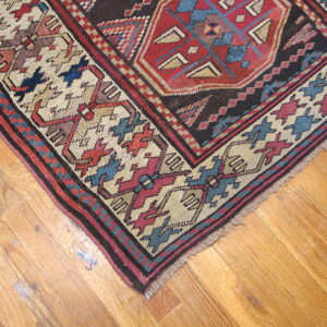 Detailed geometric rug in red, dark blue, and cream colors, showing fringe on rustic wood flooring.