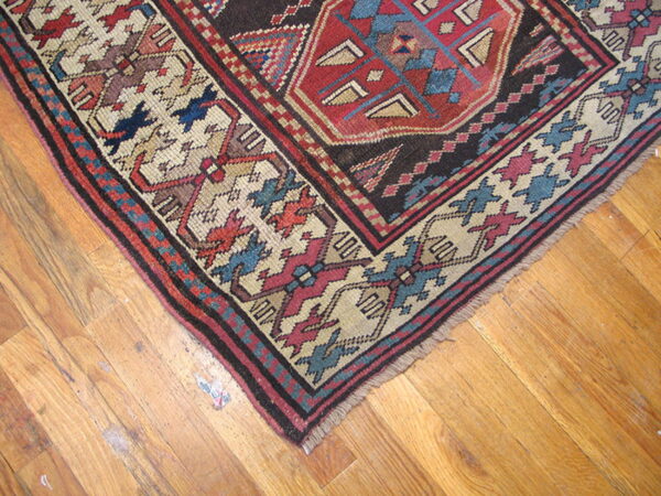 Detailed geometric rug in red, dark blue, and cream colors, showing fringe on rustic wood flooring.