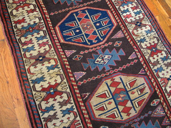 This dark brown runner rug with red and blue geometric medallions lies on polished wood flooring.